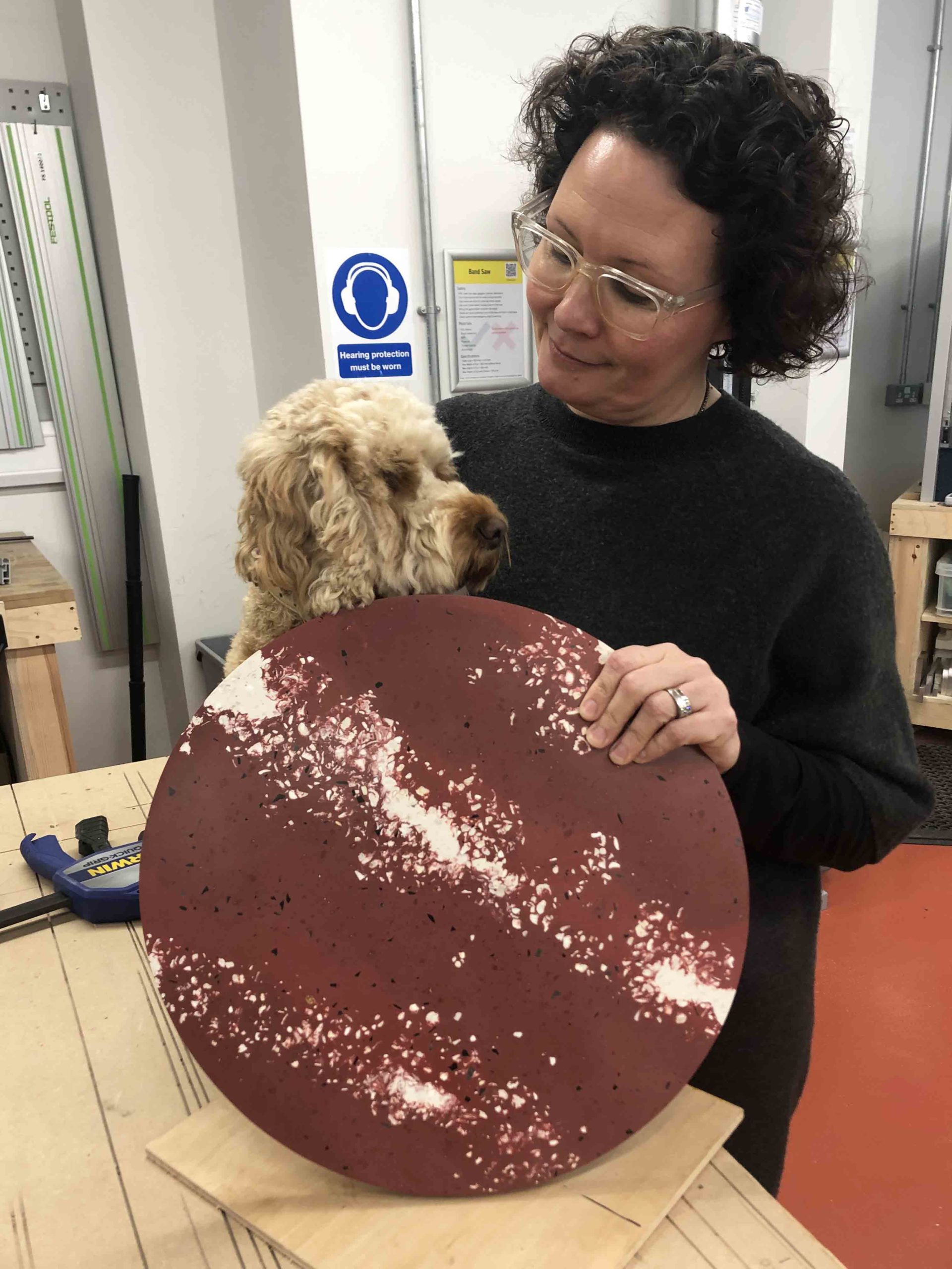 Spared workshop including margo the dog. Holding a round tabletop made from plastic waste