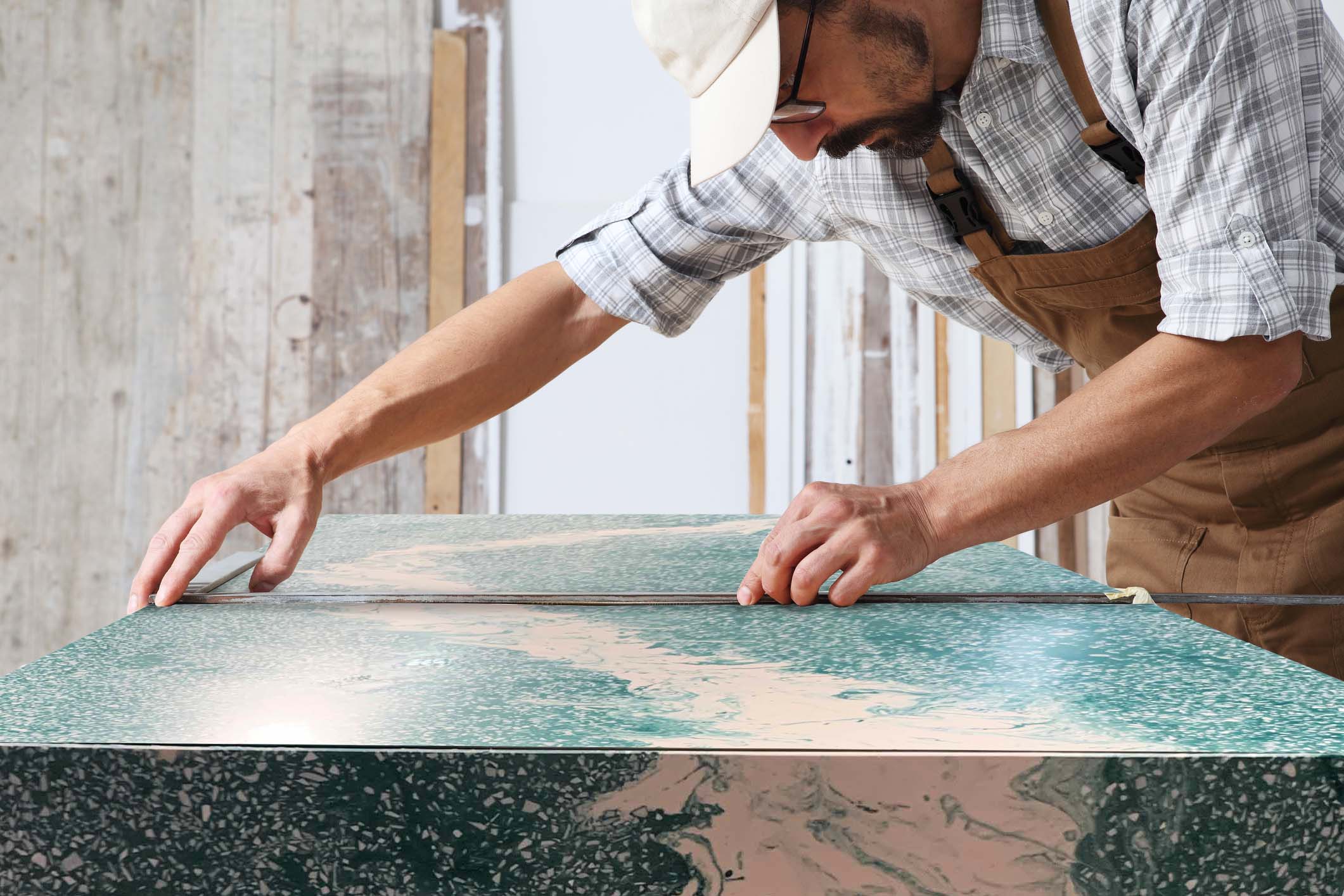Male carpenter working the wood in carpentry workshop, taking measures on wooden door with a metal square ruler on a wooden door, wearing overall and cap